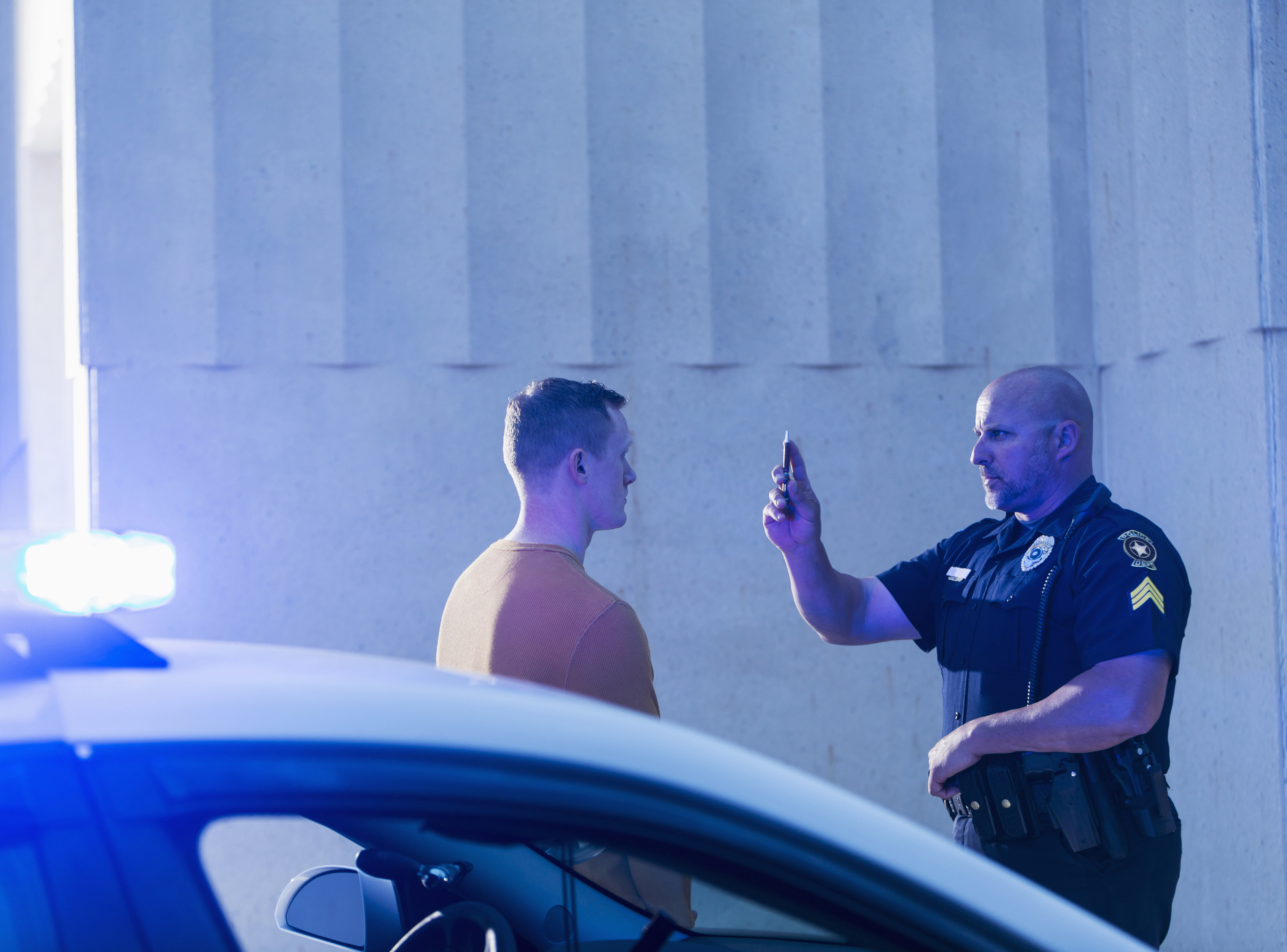 Police officer giving sobriety test to young man, with a police cruiser in the foreground, photo by kali9/Getty Images