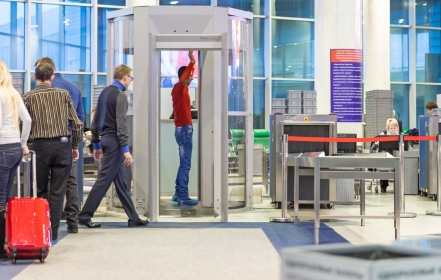 Passengers wait to enter the xray machine as a man is scanned at an airport,