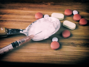 Pills, spoon with white powder, and syringe on a wooden surface, photo by mbruxelle/Adobe Stock