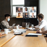 People wearing masks in a conference room on a call with remote colleagues, photo by Prostock-studio/Adobe Stock