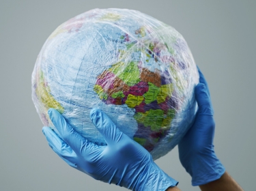 Gloved hands holding a globe wrapped in plastic, photo by nito/Adobe Stock