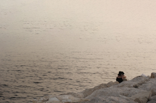 Two people embrace while sitting on a rocky shoreline and looking across the horizon, Antelias, Lebanon, May 2009