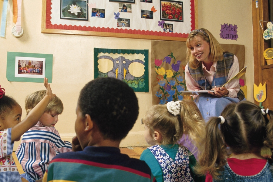 Preschool or kindergarten student raising her hand as teacher reads a book