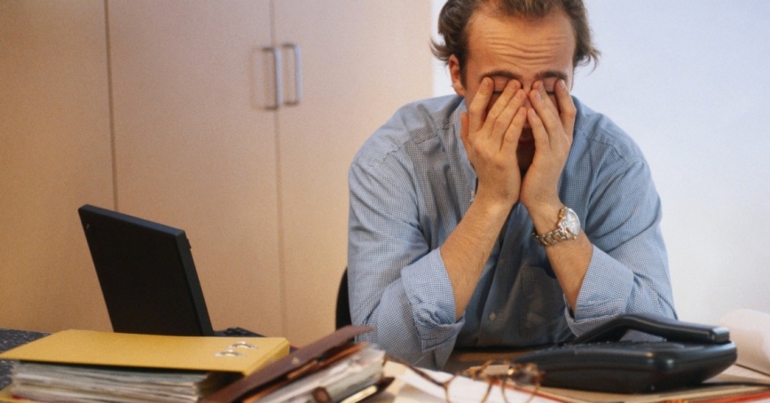 A man stressed in his office covering his eyes