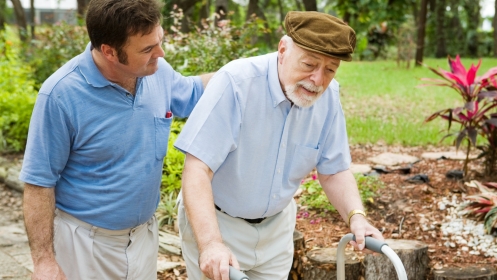 A younger man helping an elderly man who is using a walker