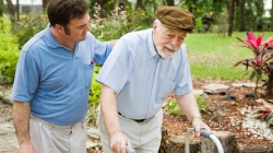 A younger man helping an elderly man who is using a walker