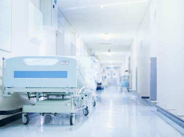 Hospital bed in a hospital corridor, photo by PeopleImages/Getty Images