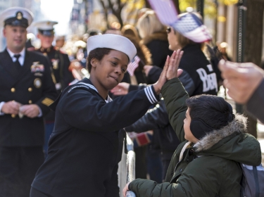 Navy Petty Officer 3rd Class Zatyra Rousseau high-fives a child during the 2018 Veterans Day Parade in New York City, Nov. 11, 2018.