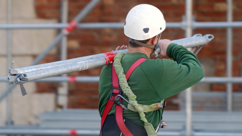Male construction worker in hard hat carrying pipes