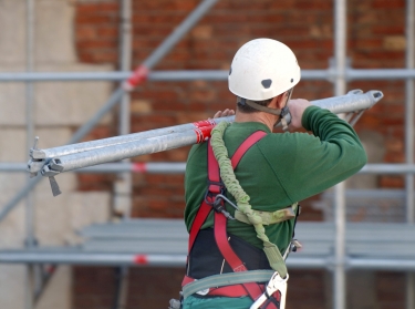 A construction worker in a hard hat carrying pipes