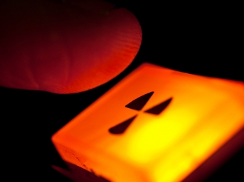 Jari melayang di atas tombol yang menyala dengan tanda peringatan radiasi, foto oleh davidhills/Getty Images