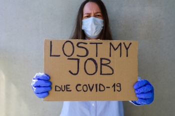 Seorang wanita mengenakan topeng dan sarung tangan memegang tanda yang mengatakan dia kehilangan pekerjaannya karena COVID-19, foto oleh tataks/Getty Images