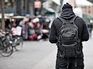 Hooded lone wolf man wearing black carrying bag in urban public setting, photo by Lorado/Getty Images