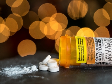 Close up of a prescription bottle with Oxycodone label and white pills spilling out, photo by BackyardProduction/Getty Images