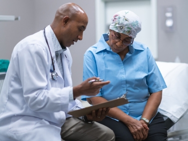 Doctor holding a clipboard and consulting with an older female cancer patient, photo by FatCamera/Getty Images