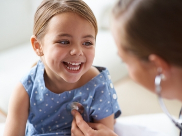 Little girl smiling at doctor listening to her heartbeat with a stethoscope, photo by PeopleImages/Getty Images