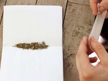 Hands holding rolling paper and filter over a table with a mix of marijuana and tobacco on white paper