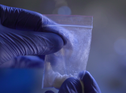 A person wearing blue gloves conducts a forensic analysis of synthetic opioids.