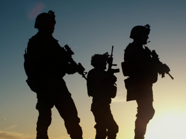 Soldiers in military gear are silhouetted against the setting sun.