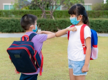 Two children wearing backpacks bump elbows as a greeting during the COVID-19 pandemic, photo by ake1150sb/Getty Images