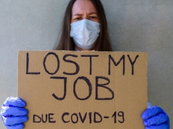 A woman wearing a mask and gloves holds a sign that says she lost her job due to COVID-19, photo by tataks/Getty Images