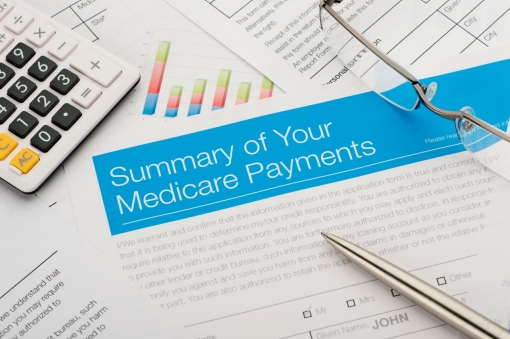 Medicare payments summary on top of other paperwork, with glasses and calculator