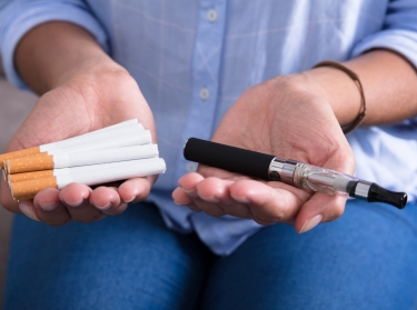 Hands holding electronic vaping device and cigarettes, photo by AndreyPopov/Getty Images