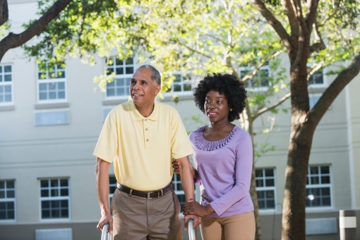 A young African American woman helping her father using a walker