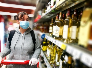Woman with a shopping cart wearing a mask and gloves in the alcohol aisle at the grocery store, photo by coldsnowstorm/Getty Images