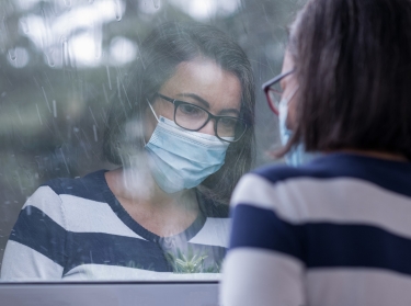 Woman wearing a face mask looks out a window in the rain, photo by FerreiraSilva/Getty Images