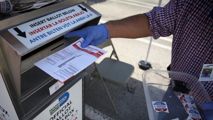 A poll worker casts a mail-in ballot for a voter at a drive-thru polling station during the primary election amid the COVID-19 outbreak in Miami, Florida, August 18, 2020, photo by Marco Bello/Reuters