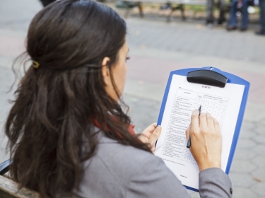 Woman sits on park bench filling out survey, photo by DW labs Incorporated/Adobe Stock