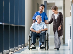 Orderly pushing man in wheelchair down hospital hall