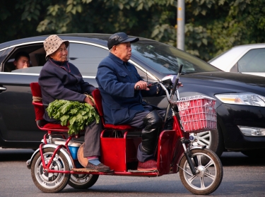 An elderly couple carrying vegetables ride a tricycle along a street in Beijing, October 17, 2013