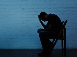 Depressed man sitting in a chair silhouetted against a brick wall