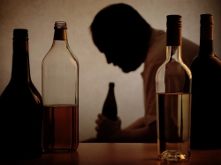 Silhouette of a man drinking behind bottles of alcohol in the foreground