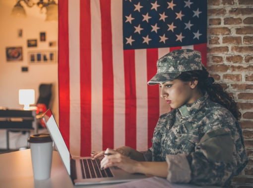 Young female soldier working on a laptop with United States flag in the background