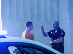 Police officer giving sobriety test to young man, with a police cruiser in the foreground