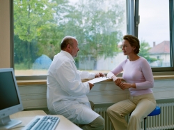Male doctor sitting with a female patient near a widow, clipboard in hand