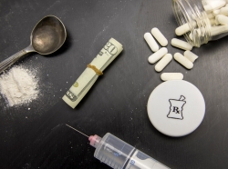 Opioids in pill, powder, and syringe on chalkboard with rolled twenty dollar bill