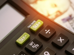 Close up of calculator buttons for tax increase or tax decrease with blurred American dollars in the background