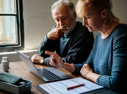 Woman and elderly man looking at a laptop with insurance forms on the table nearby