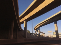 Freeway ramps viewed from underneath, against a blue sky.