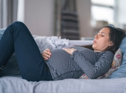 Pregnant woman lying on a couch, photo by Fly View Productions/Getty Images
