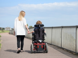 Woman walking next to, and holding hands with, her son in a wheelchair, photo by JohnnyGreig/Getty Images