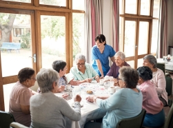 Staff person talks to a group of women dining at a nursing home, photo by shapecharge/Getty Images