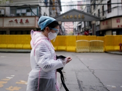 A woman wearing a face mask walks through a residential area blocked by barriers in Wuhan, Hubei province, April 3, 2020, photo by Aly Song/Reuters