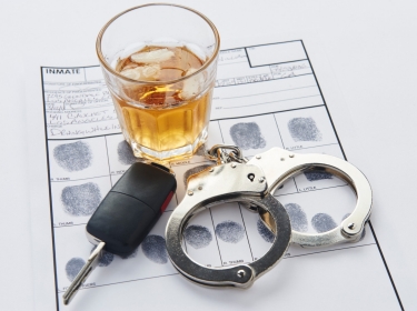Glass of alcohol, keys, and handcuffs on top of an arrest record with fingerprints, photo by TheCrimsonRibbon/Getty Images