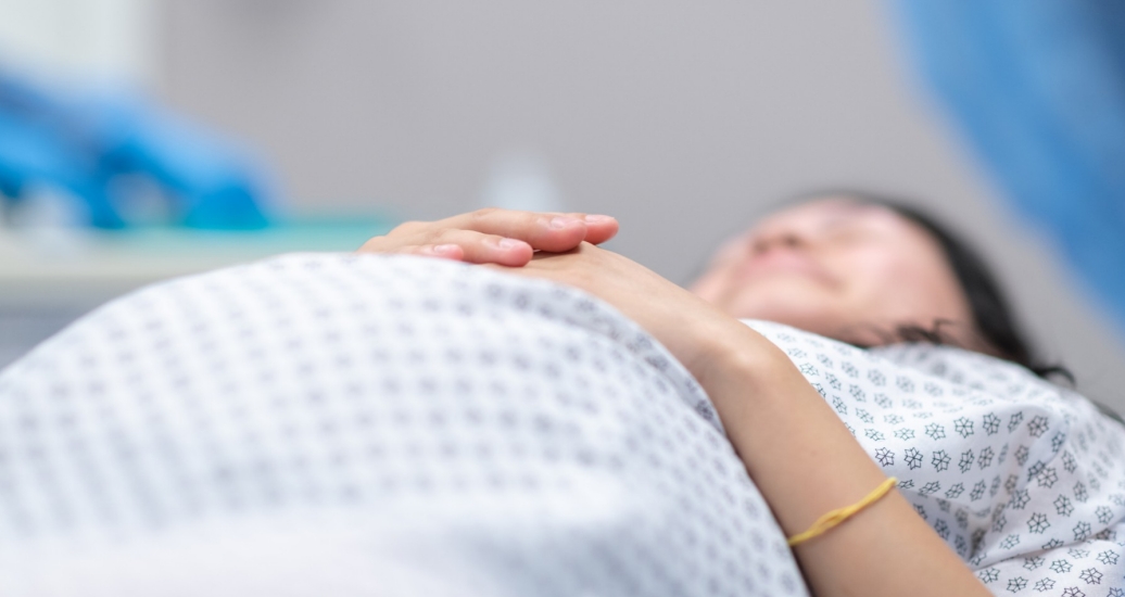 Close up of a pregnant woman in a hospital gown laying down, photo by FatCamera/Getty Images
