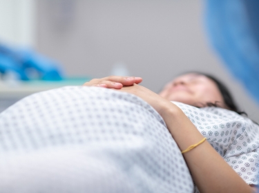 Close up of a pregnant woman in a hospital gown laying down, photo by FatCamera/Getty Images